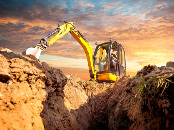 Mini Excavator. Yellow mini excavator on the construction site. Excavator operator chooses the ground for the foundation. Mini digger digs down in the background of the sunset.